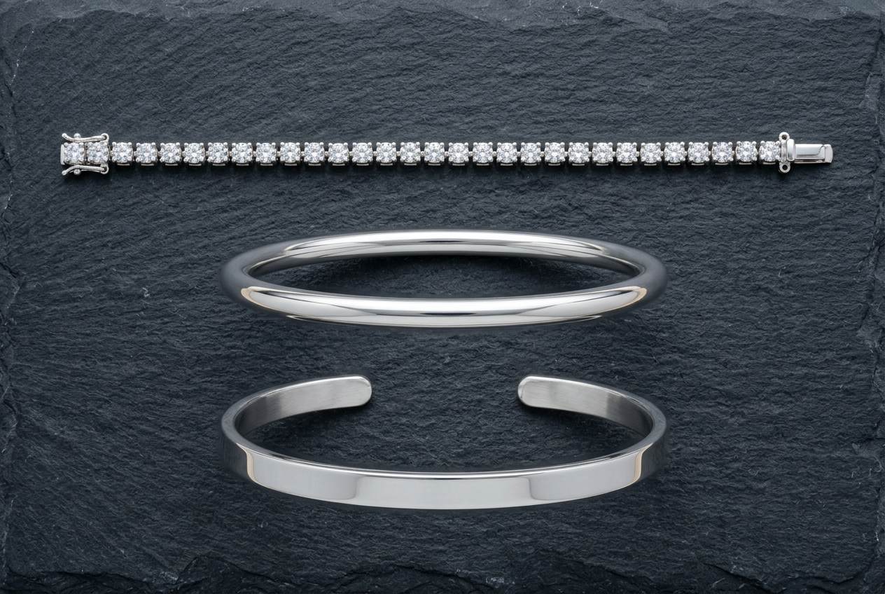 Three sterling silver bracelets on dark slate: a flexible stone-set tennis line, a rigid closed bangle and an open cuff