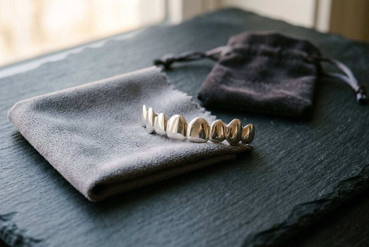 Silver custom grillz resting on a soft polishing cloth beside a storage pouch