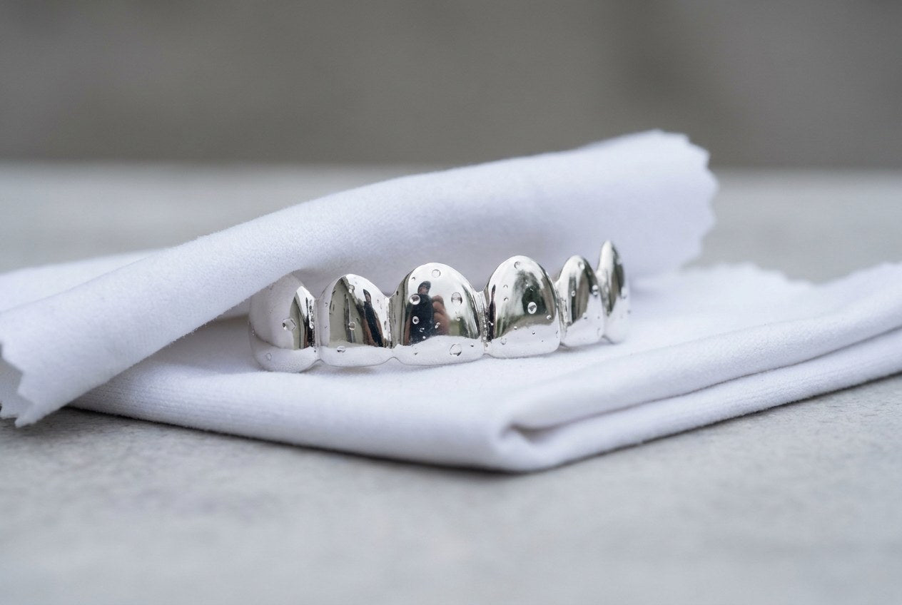 Polished silver grillz being patted dry on a folded lint free cloth on a clean surface