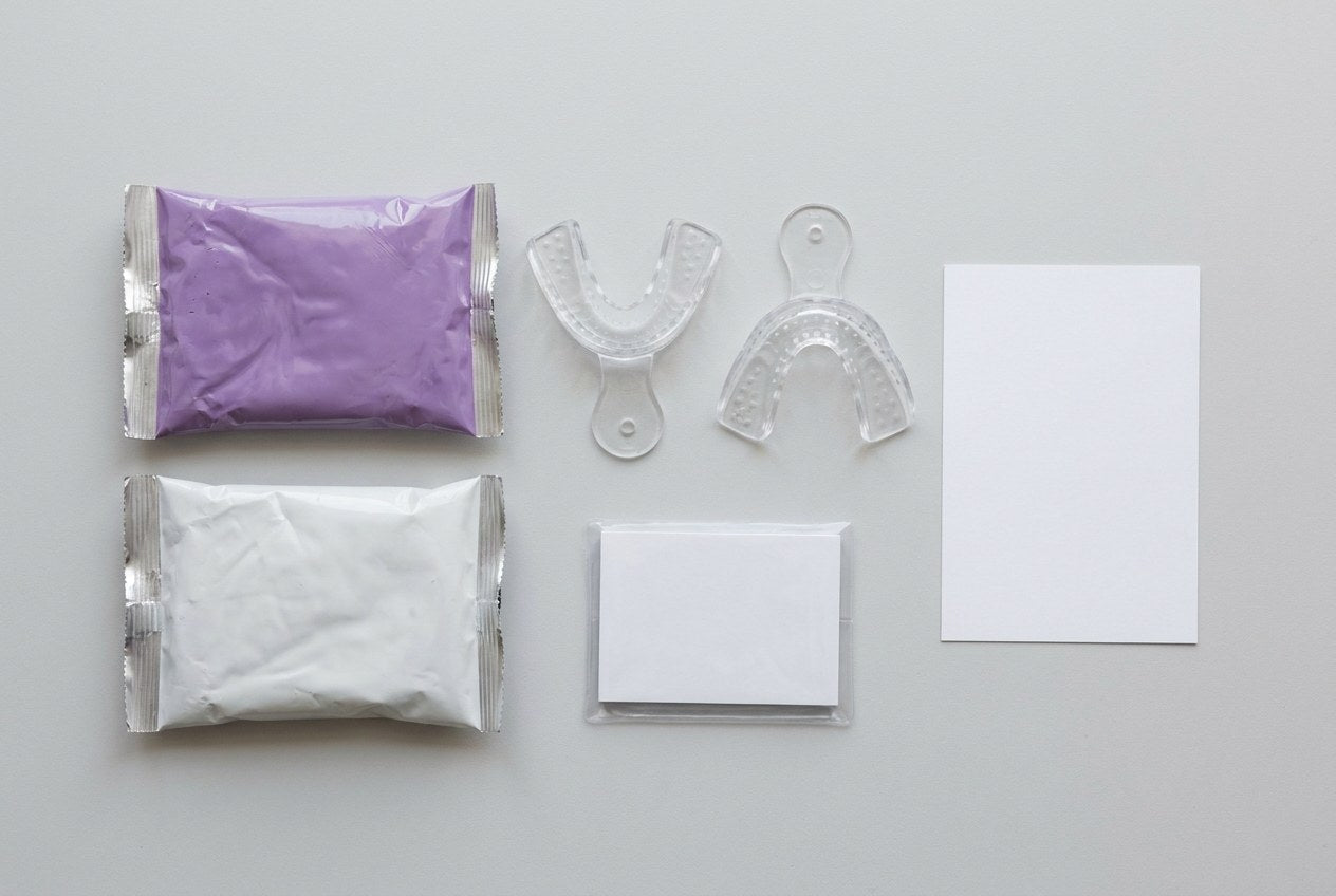 Flat lay of a dental impression kit showing two clear trays, sealed putty pouches and an instruction card