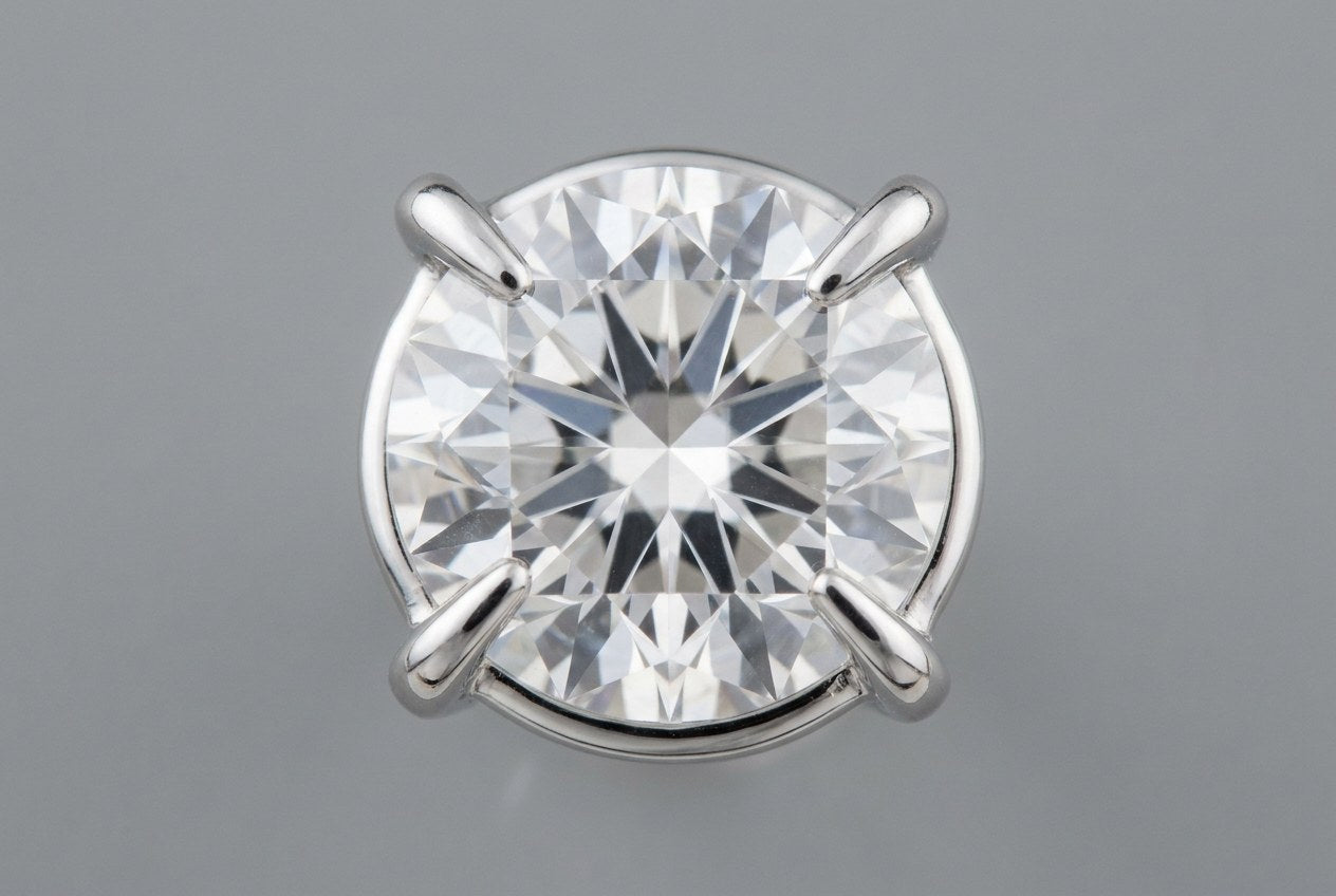 Macro close-up of a round moissanite held by four evenly matched prongs pressed flat against the stone