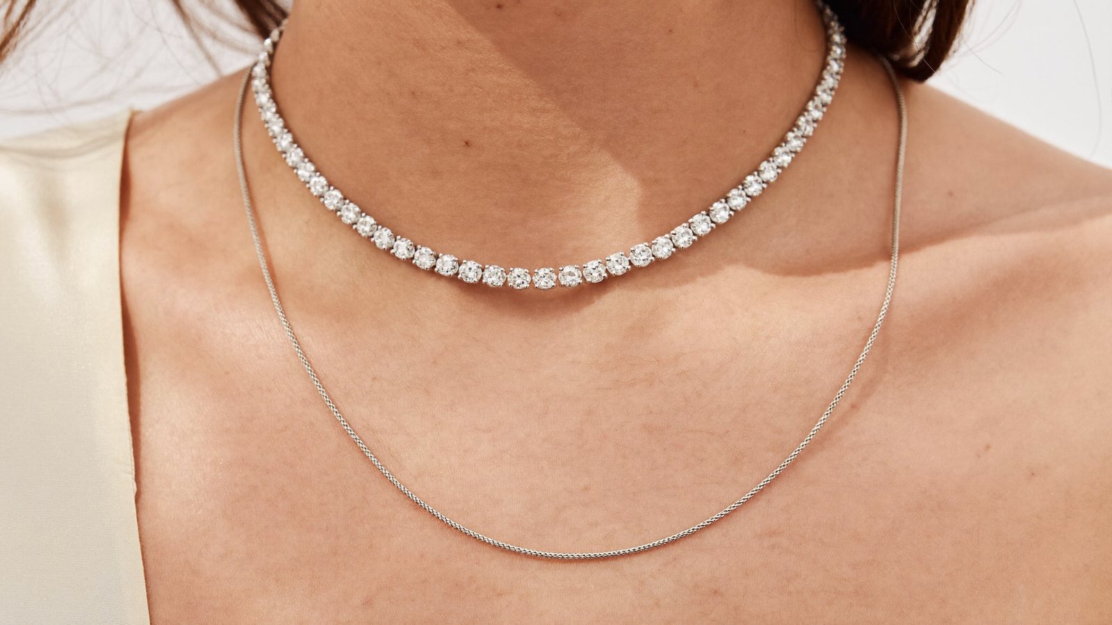 Moissanite tennis chain layered with a plain sterling silver chain at the collarbone