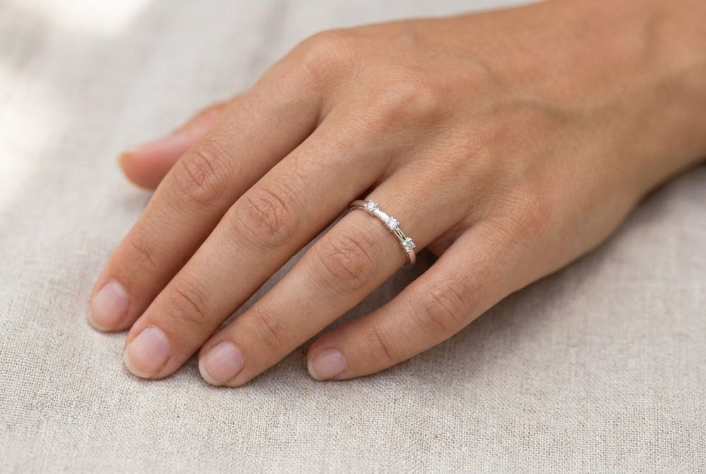 Slim sterling silver band ring set with small moissanite stones worn on a hand resting on linen in daylight