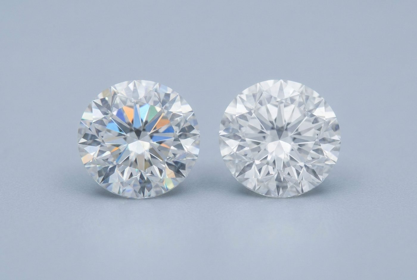 Two round brilliant cut colorless stones side by side, the left showing more colored fire and the right a whiter sparkle