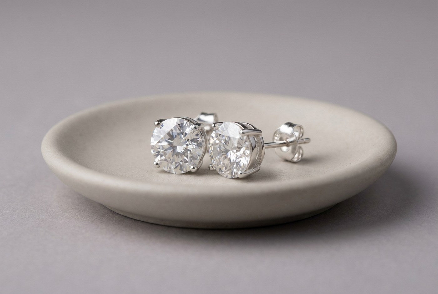 Round moissanite stud earrings in sterling silver with a butterfly back resting on a small ceramic dish