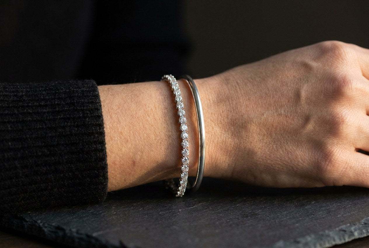 A slim moissanite tennis bracelet stacked next to a plain sterling silver bangle on a wrist