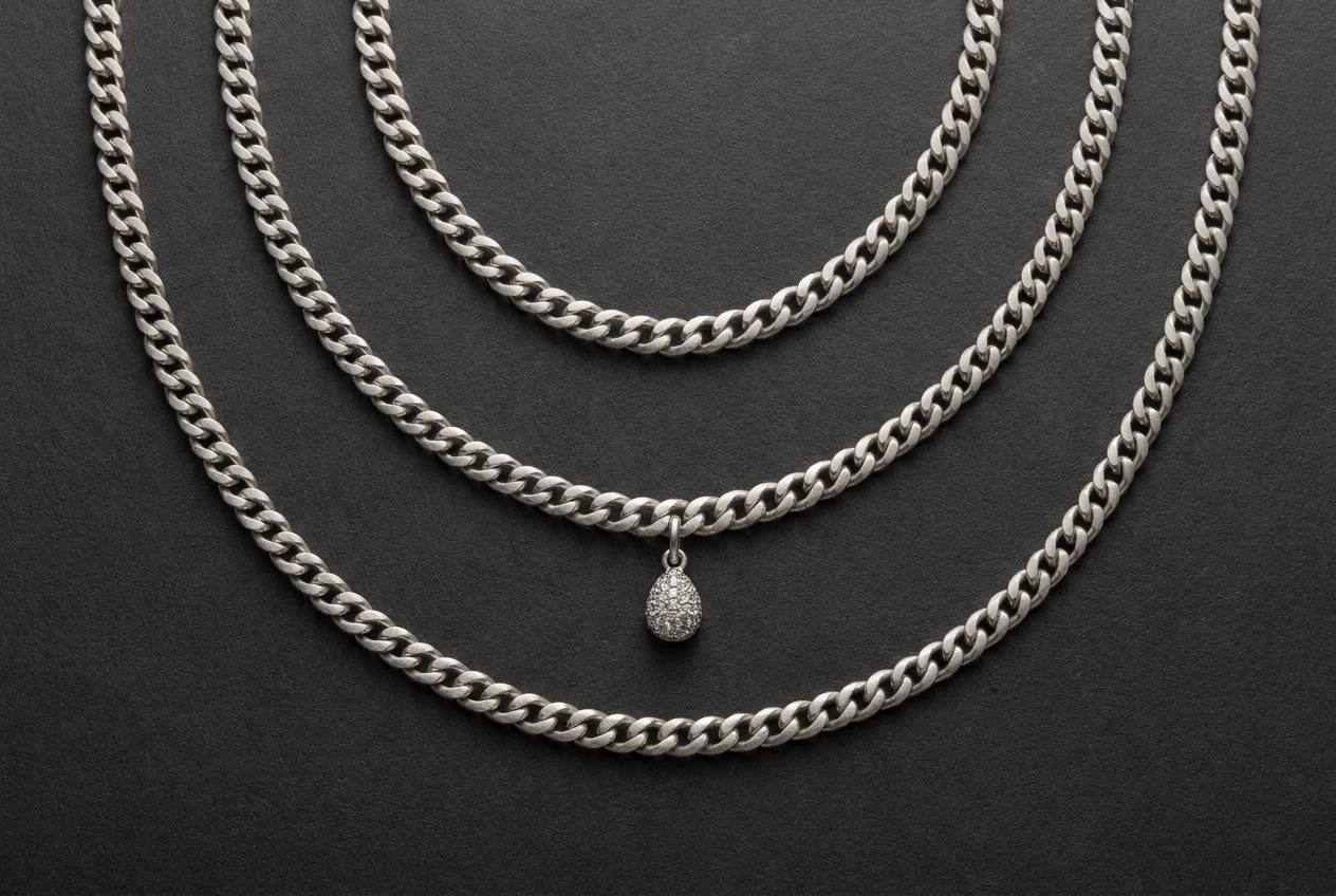 Three silver chains laid out at three different lengths with a small pendant hanging from the middle chain