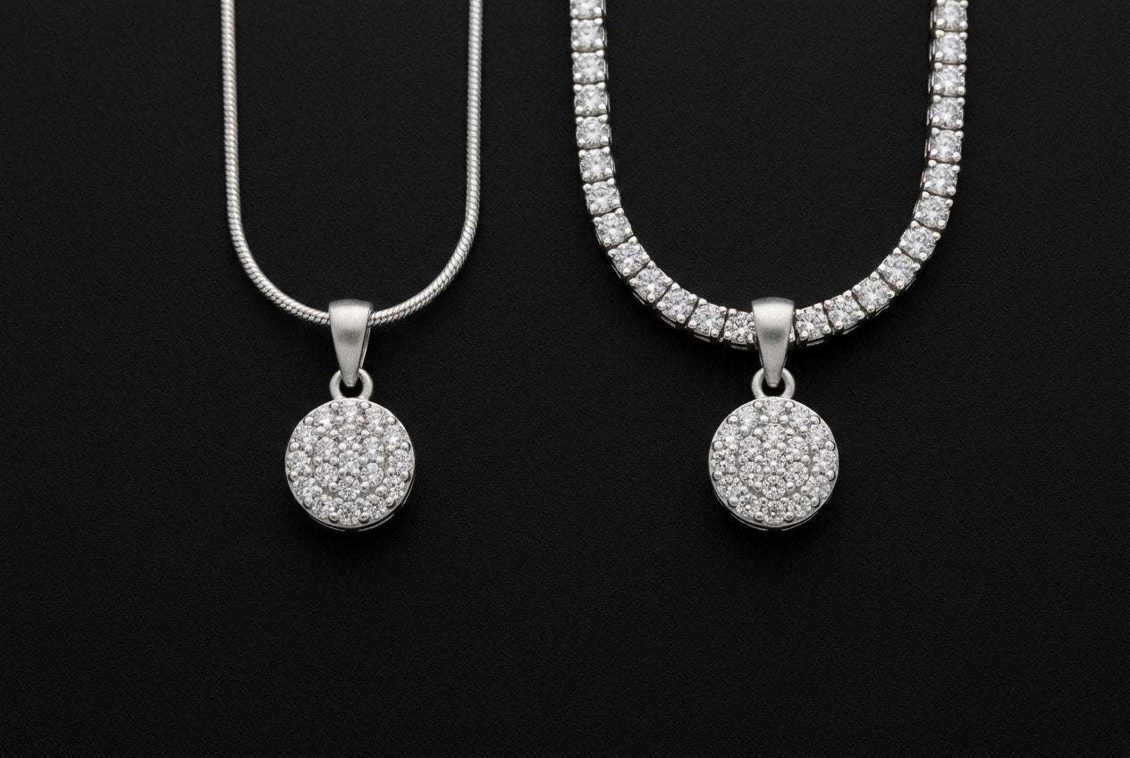 Two identical silver pendants side by side, one on a thin plain chain and one on a wide stone set tennis chain