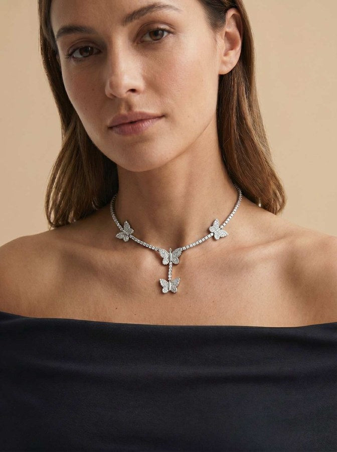 A woman wearing the Butterfly 'Dreamline' Tennis Chain featuring sparkling butterfly-shaped accents on a delicate silver tennis chain against a neutral background.