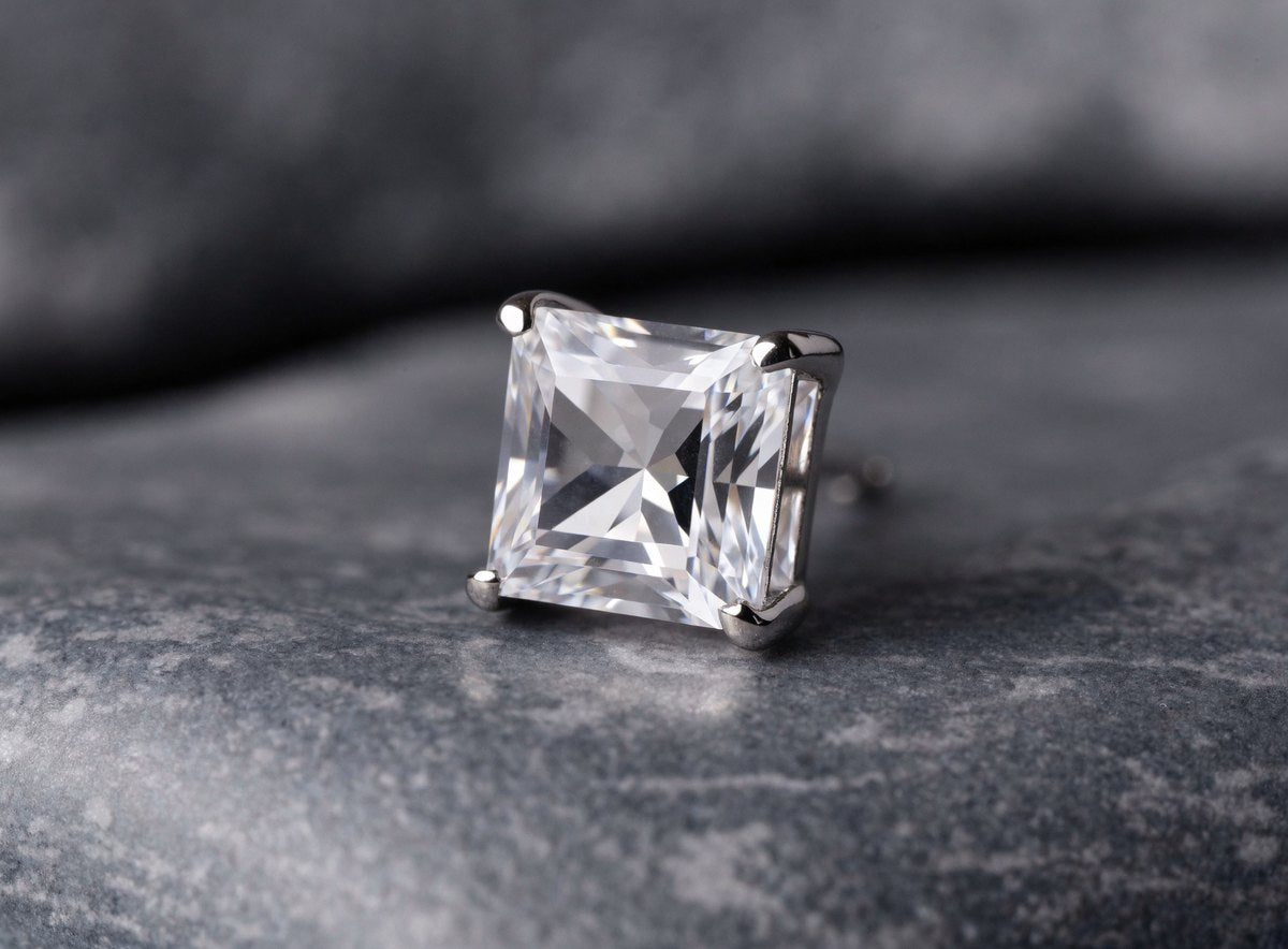 Close up of a single princess cut stone stud earring held in four silver prongs