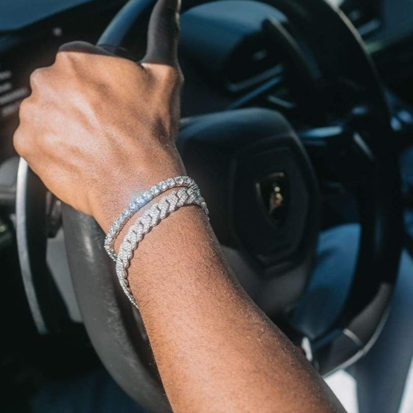 Hand holding a steering wheel with a diamond bracelet on, inside a car.