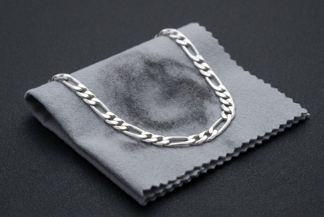 A silver polishing cloth darkened from use, with a sterling silver chain resting on it