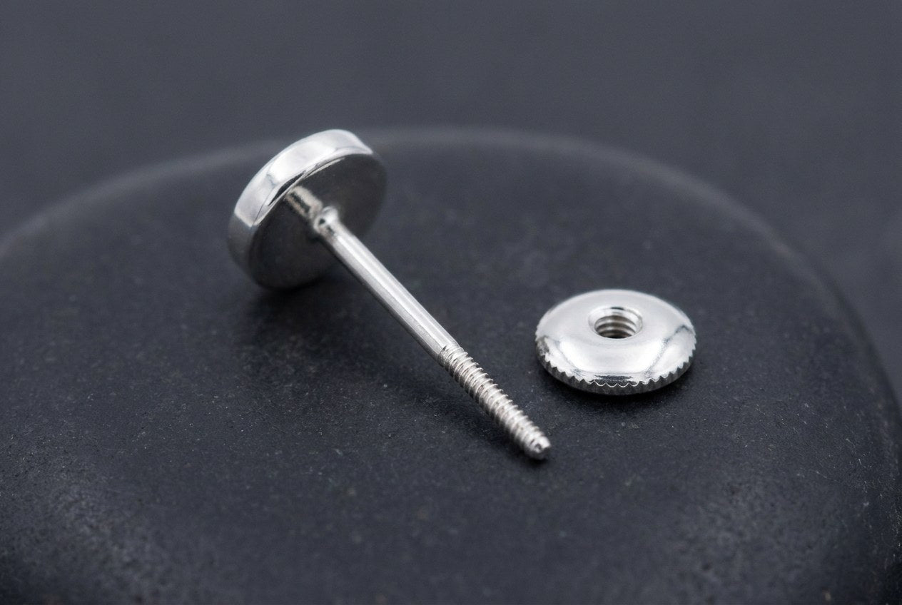 A sterling silver earring post with a threaded tip lying beside its round screw-back nut