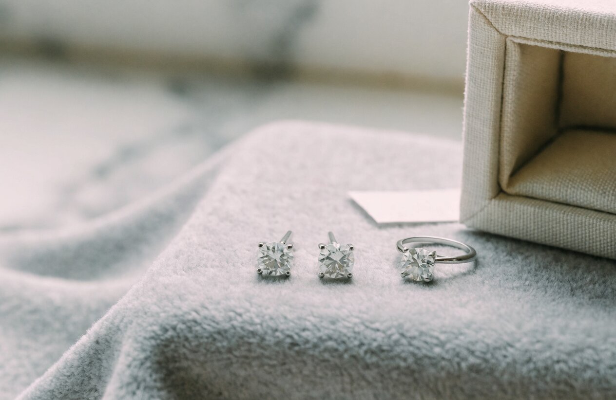Dry sterling silver moissanite studs and a ring resting on a microfiber cloth beside a fabric-lined jewelry box and an anti-tarnish strip