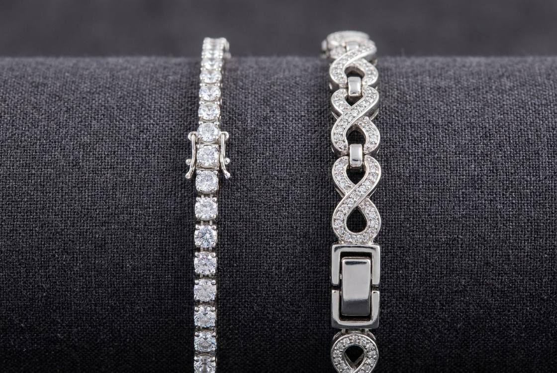 A slim moissanite tennis bracelet lying beside a heavier paved infinity link bracelet on a dark surface