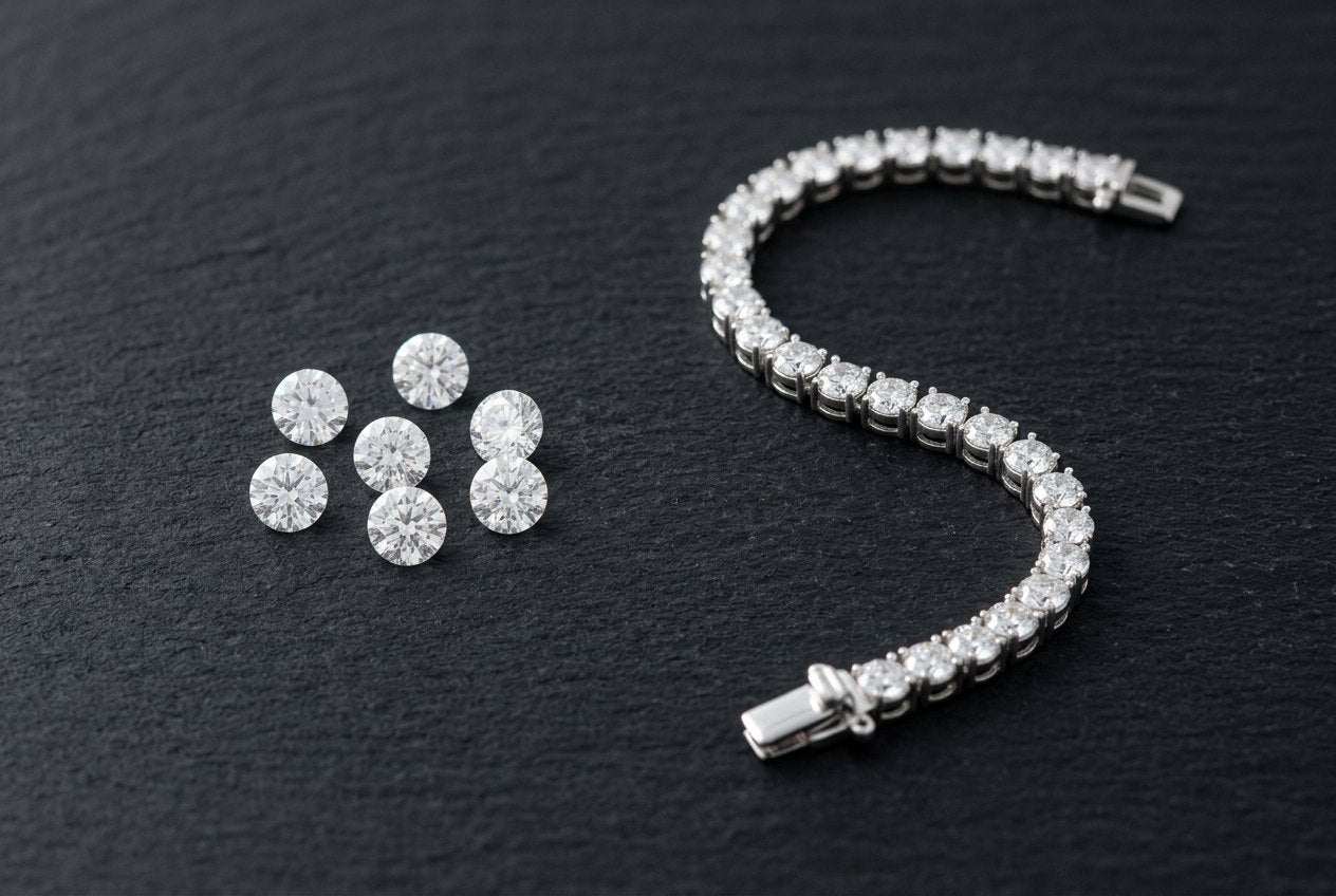 Loose colorless round moissanite stones beside a finished sterling silver tennis bracelet on a dark surface
